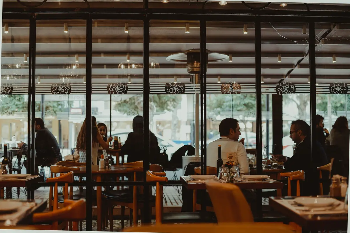 Diners at several tables, seen from across a restaurant through a glass wall, with no one in close-up.