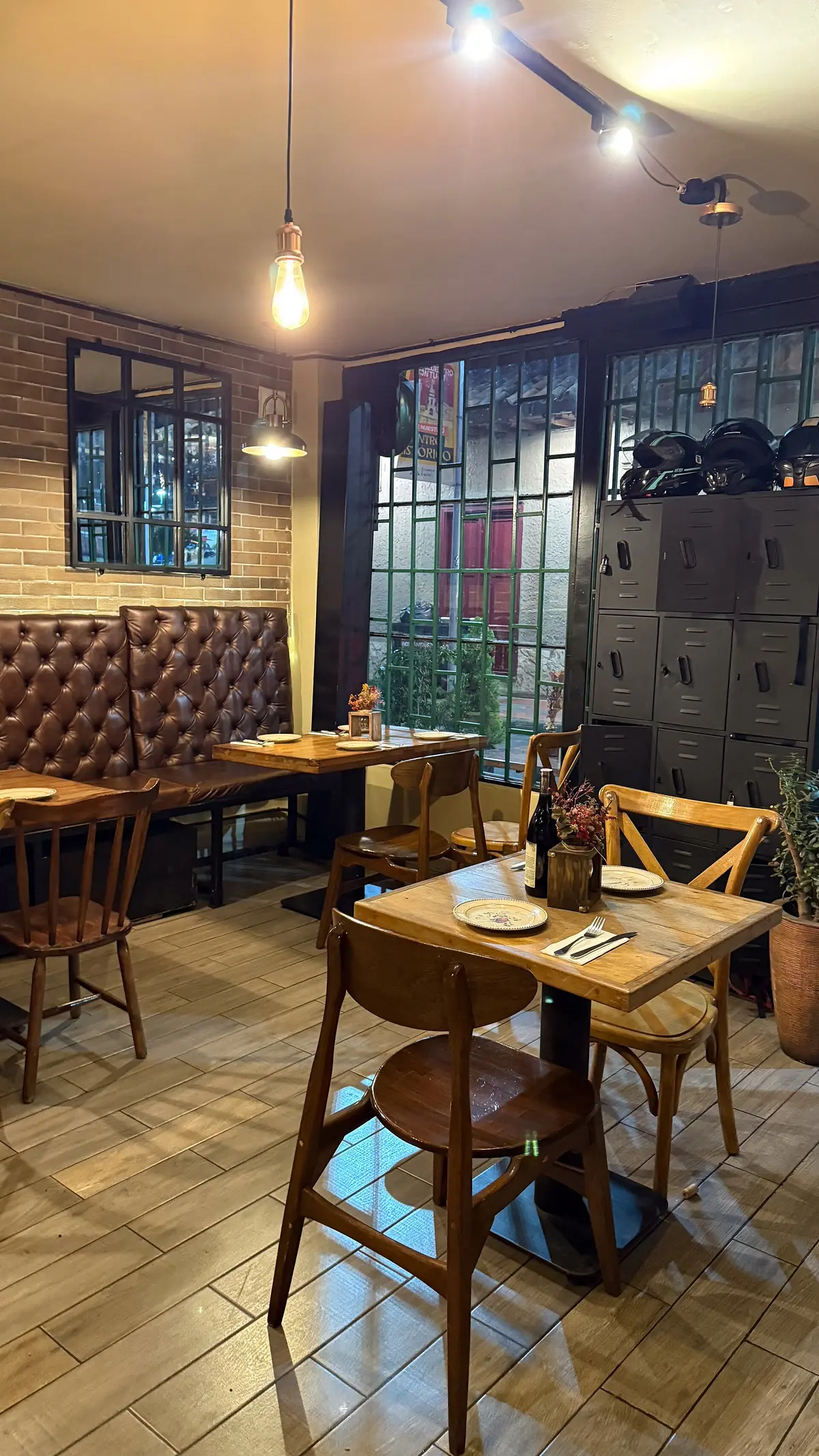A dining room with wooden tables, chairs and a long brown leather booth, plates and cutlery set out.