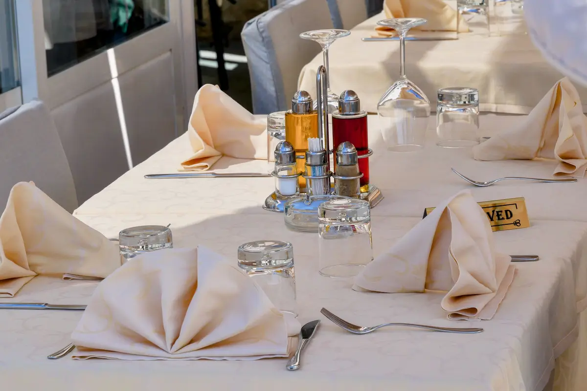 A long table with white cloths, folded napkins and glasses, set for a group behind a small reserved card.