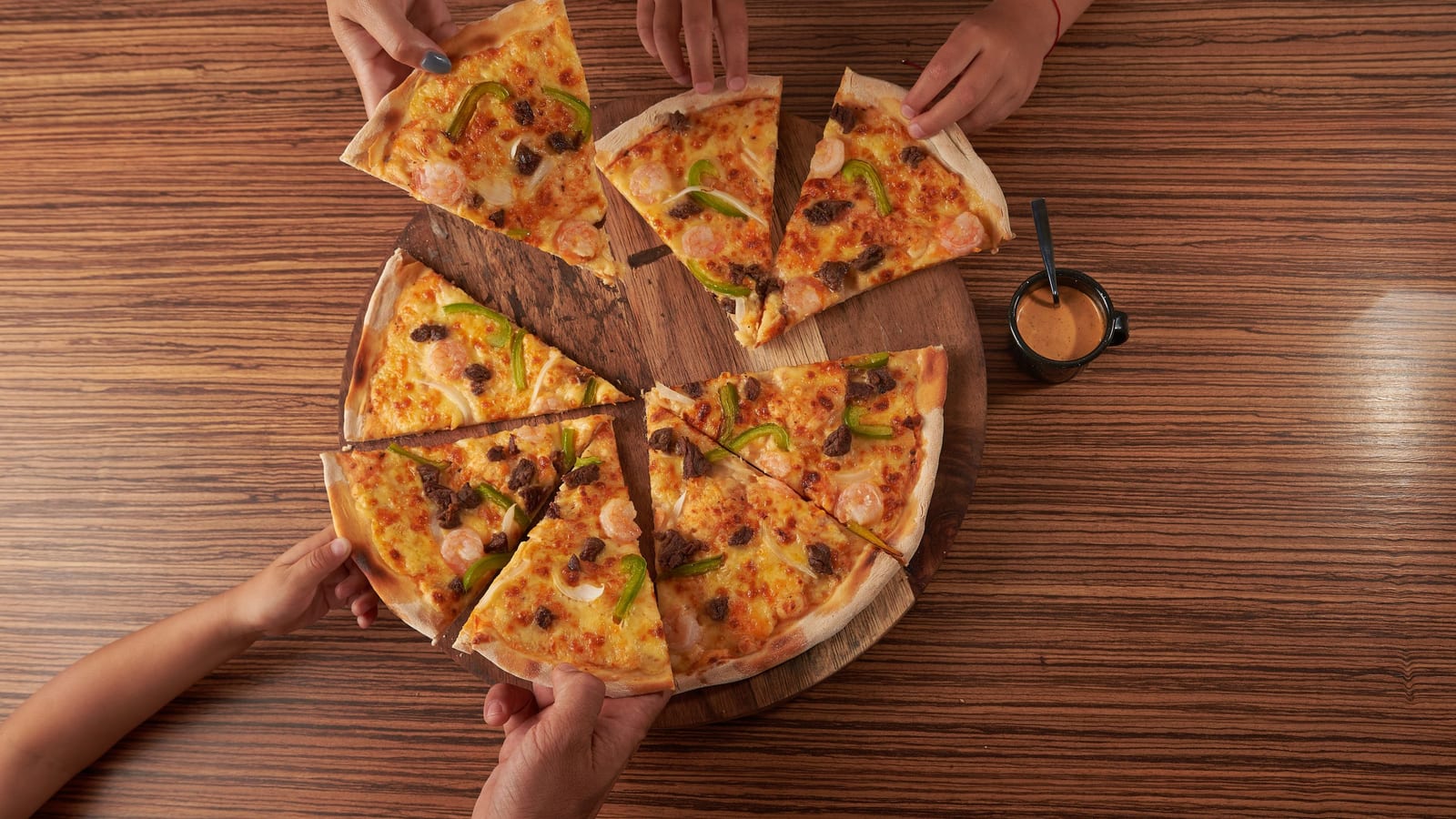 Five hands take slices of one shared pizza at a restaurant table, the kind of group dinner a giveaway can offer as its prize.