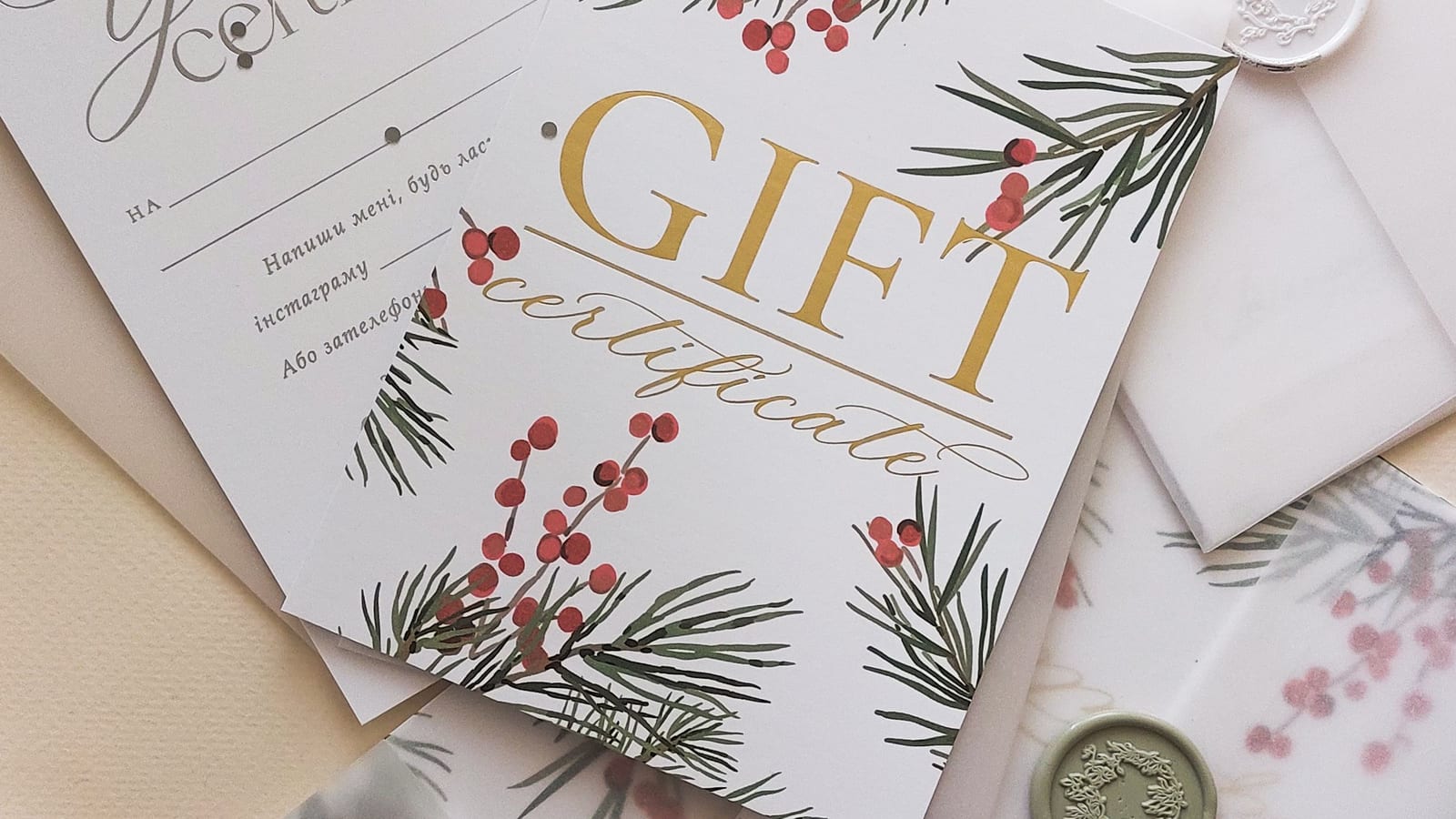 Holiday gift certificates printed with pine sprigs and red berries lie on vellum envelopes closed with wax seals.