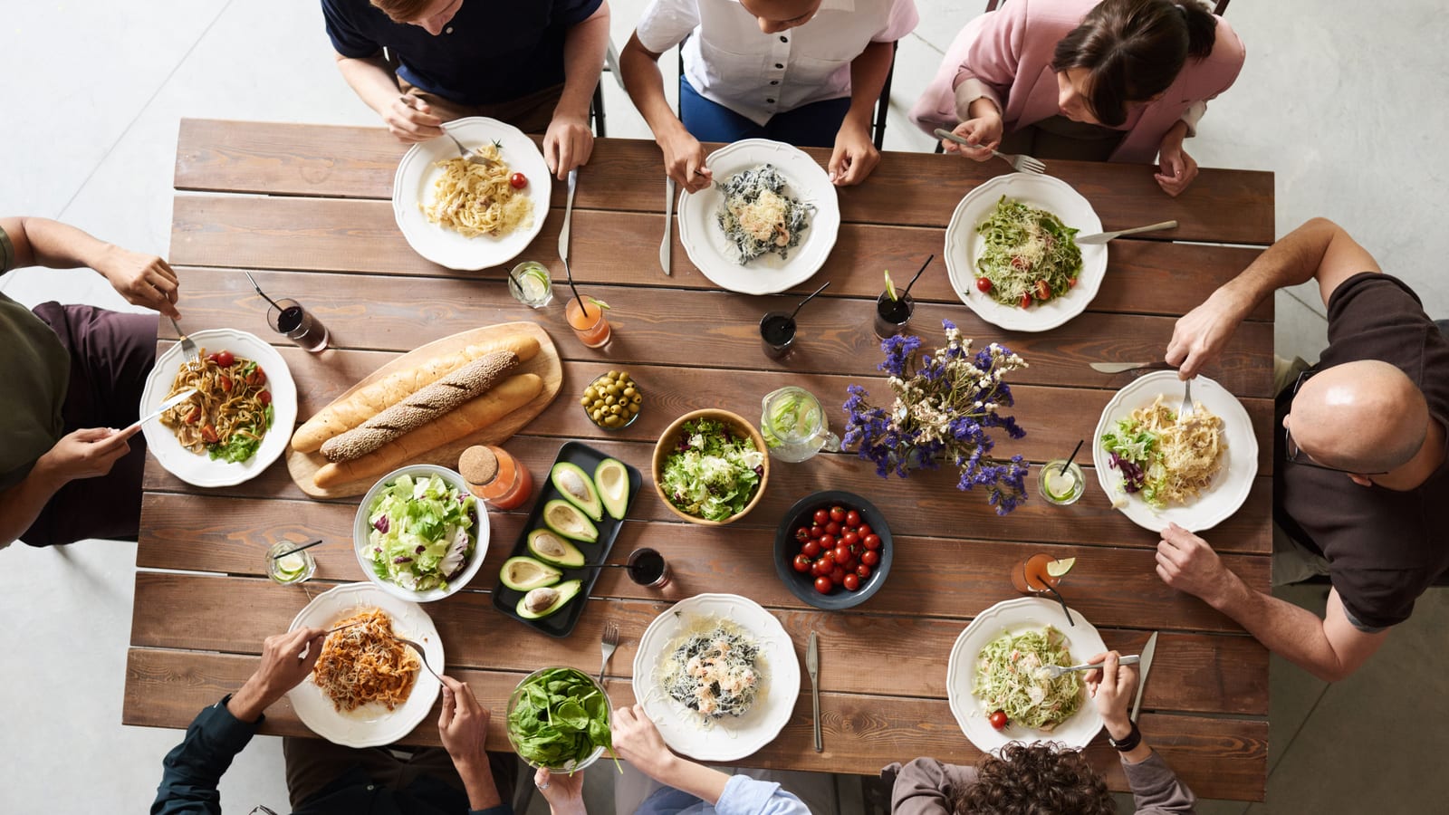 Seen from above, guests share pasta, salad and bread around one long wooden restaurant table.