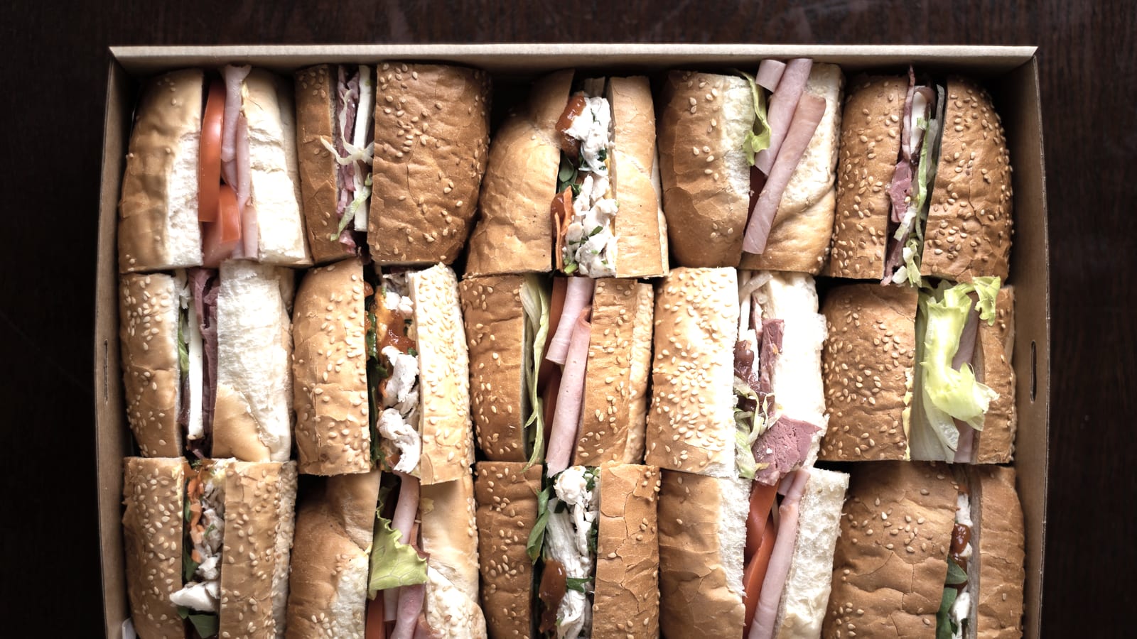 A kraft catering box packed with halved sub sandwiches, seen from above.