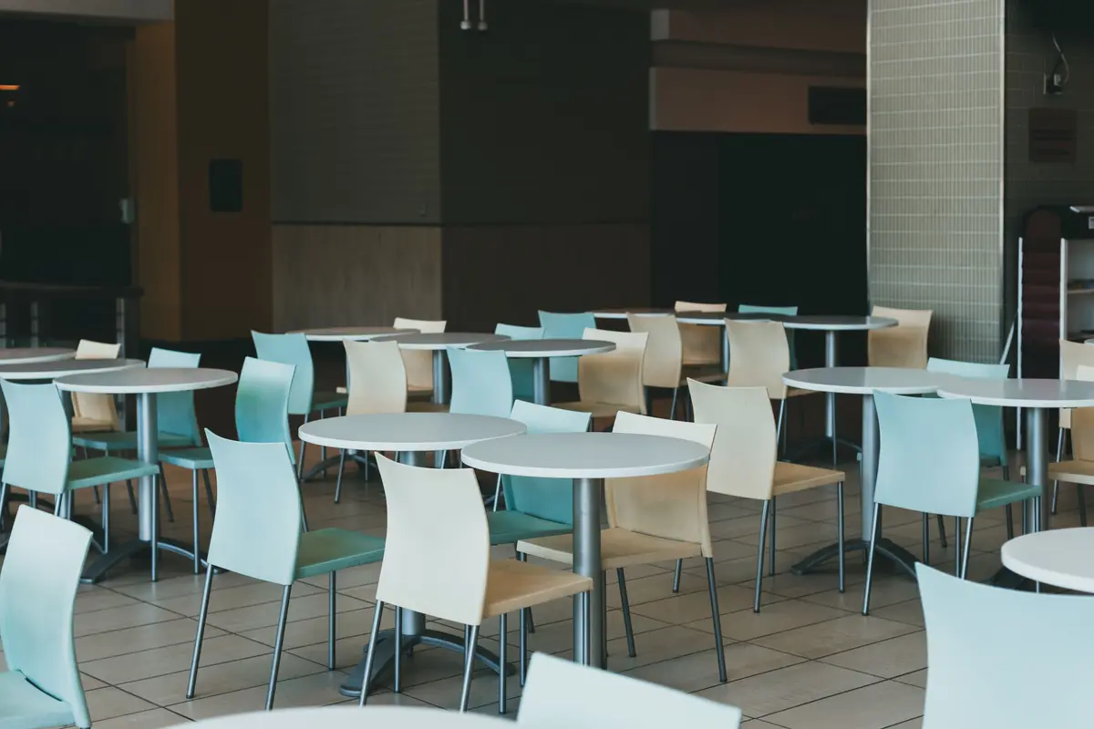 An empty dining room with round white tables and teal and cream chairs, and no guests in sight.