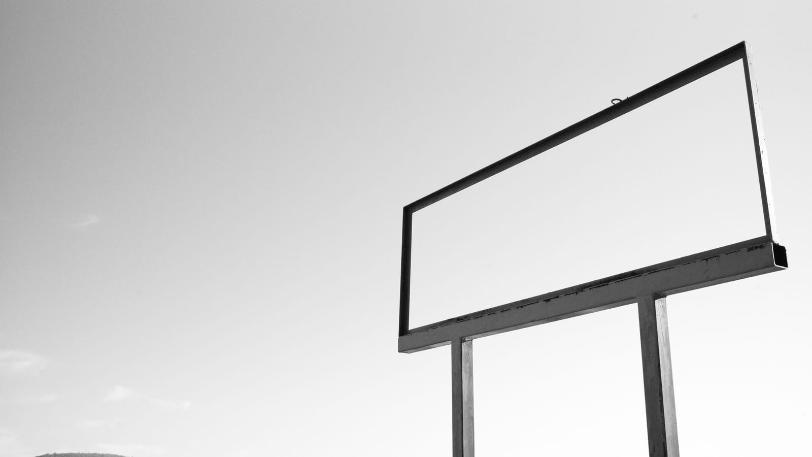 A blank billboard frame stands against a pale sky, with low hills below.