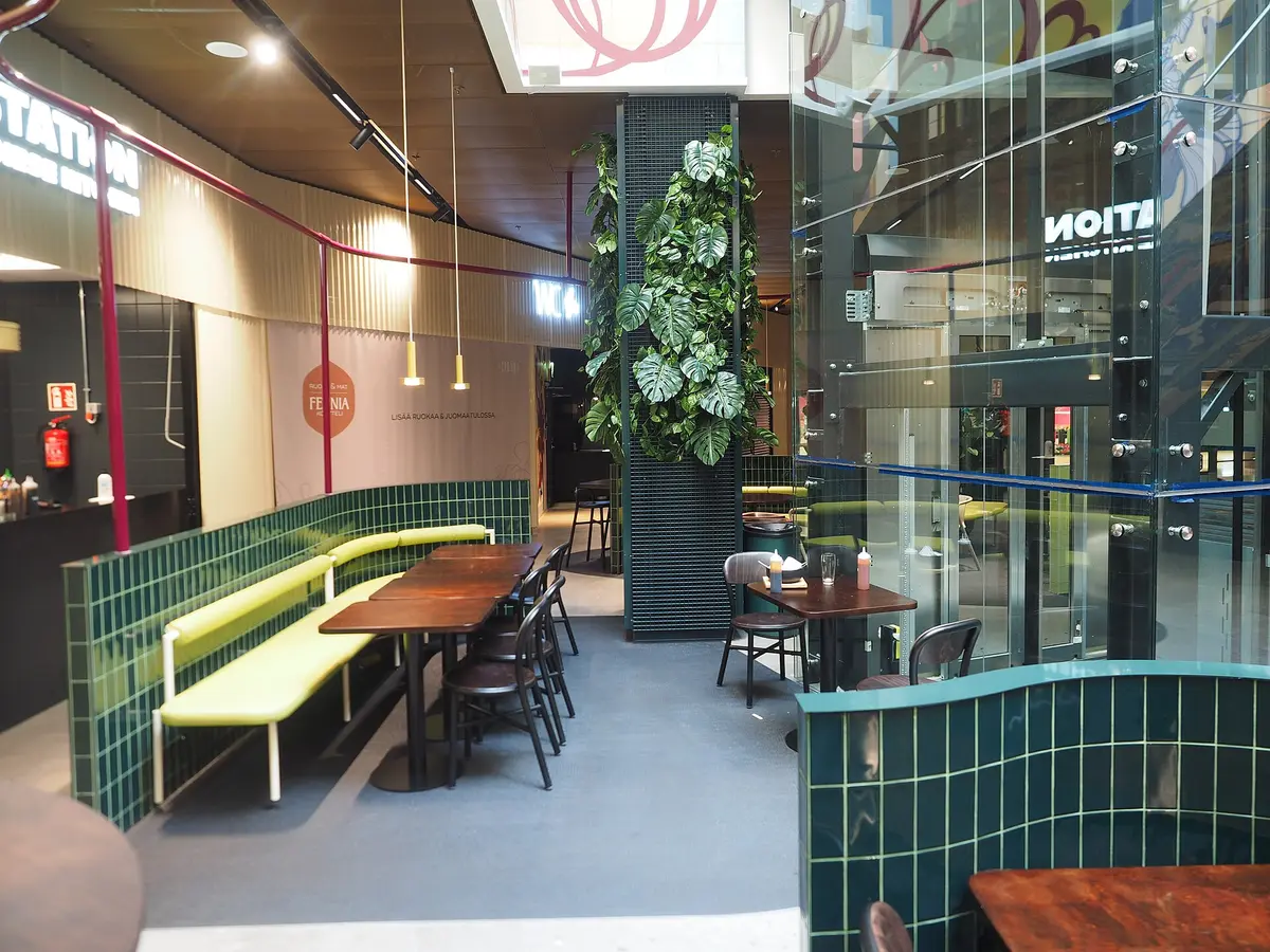 An empty dining room with dark wooden tables and chairs beside light green upholstered booths.